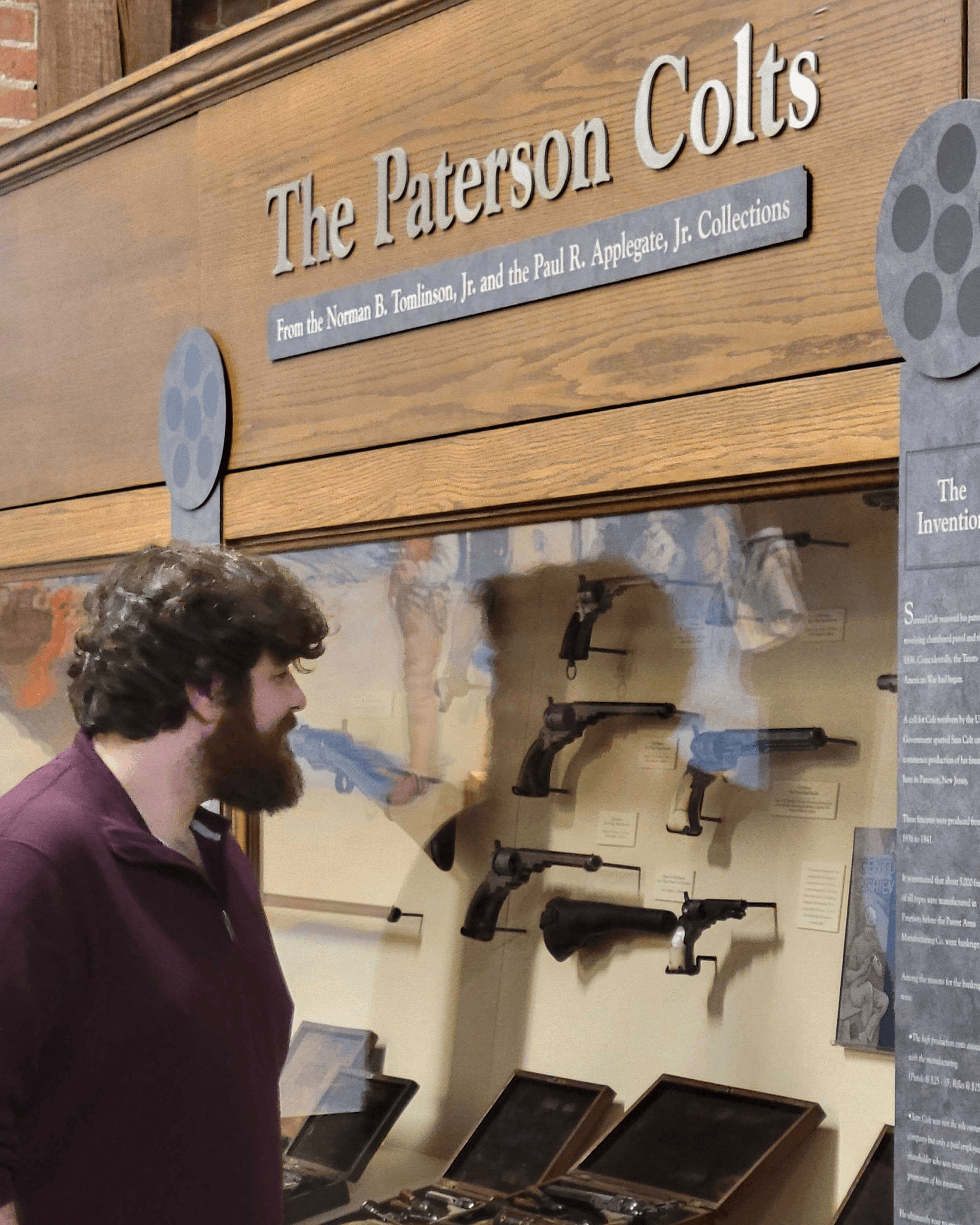 a man looking at pistols in a museum exhibit titled The Paterson Colts
